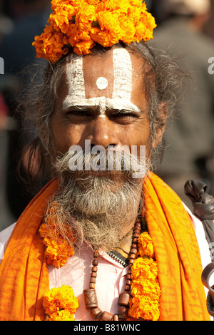 Gesicht-Portrait-Foto von einem Nepali Sadhu in orangefarbene Gewänder gekleidet, mit Bemalung und Blumen in den Haaren im Herzen von Kathmandu, Nepal Stockfoto