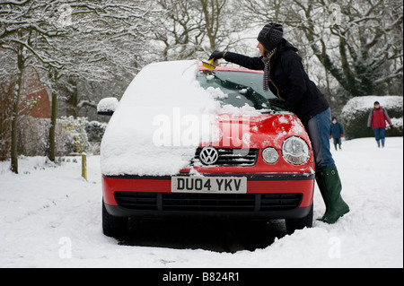 Eine Frau löscht starken Schneefall aus ihrem Auto, bevor Sie versuchen, zur Arbeit fahren. Starker Schneefall bringt Chaos für Pendler Stockfoto