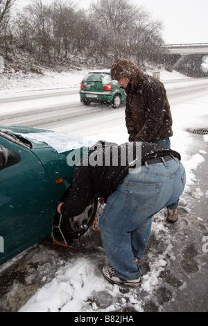 Zwei Männer versuchen zu Ketten auf dem Vorderrad eines Autos in der Mitte ein Sturm in der Schweiz setzen Stockfoto