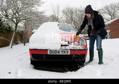 Eine Frau löscht starken Schneefall aus ihrem Auto, bevor Sie versuchen, zur Arbeit fahren. Starker Schneefall bringt Chaos für Pendler Stockfoto