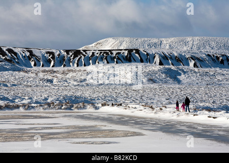 Mann mit zwei Kindern zu Fuß neben zugefrorenen See im Winter mit alten Kohle verwöhnen Tipp hinter Blorenge Wales UK Stockfoto