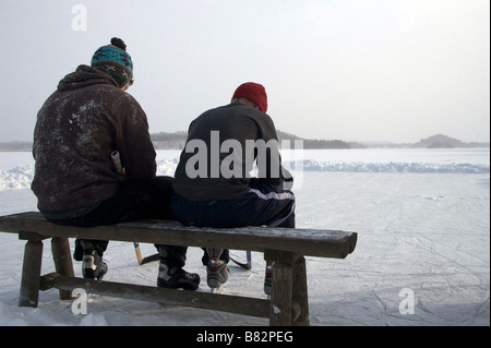 Zwei Jungs sitzen auf der Bank neben der Eisbahn Stockfoto