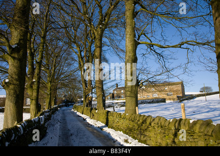 Eine verschneite Lane, klaren, blauen Himmel und landwirtschaftlichen Gebäuden in Oakworth, West Yorkshire Stockfoto