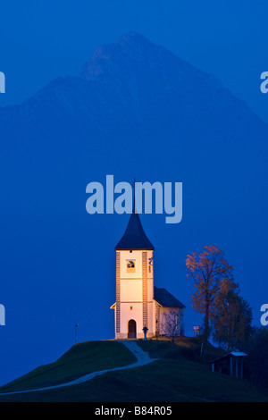 Primoz Kirche mit Storzic in Kamnik-Savinja Alpen Berg hinter Blaustich zu Kirche Hintergrund beleuchtet Stockfoto