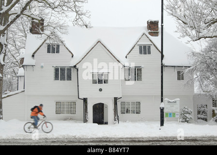 Radfahrer im Schnee: Mann Radfahren im Schnee in Bewegungsunschärfe vor White Hall, ein Haus aus dem 16. Jahrhundert und das Museum Cheam, London Stockfoto