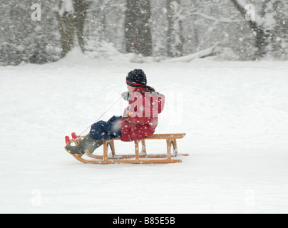 Winterspaß: kleiner Junge auf einem Schlitten in den Schnee, Cheam, Südlondon, Surrey, England Stockfoto