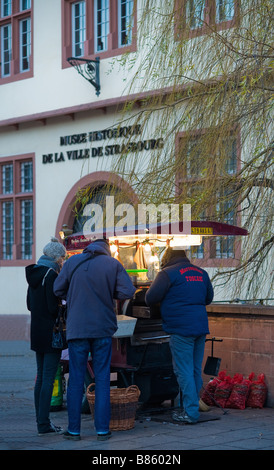 Menschen kaufen gebratene Kastanien, die durch eine Straße Verkäufer vor Historischen Museum, Winter, Straßburg, Elsass, Frankreich, Europa Stockfoto