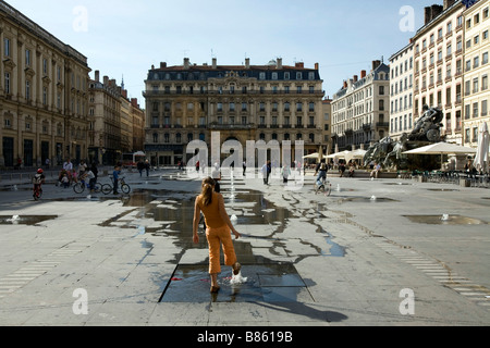 Eine Mädchen spielt mit der umstrittenen Wasserwerke der Künstler Daniel Buren am Place des Terreaux in Lyon Stockfoto