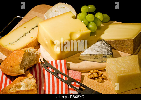 Käse mit Brot, Trauben, Walnüssen, Käsemesser und gestreifte Küchentuch auf hölzernen Platte, schwarzer Hintergrund Stockfoto