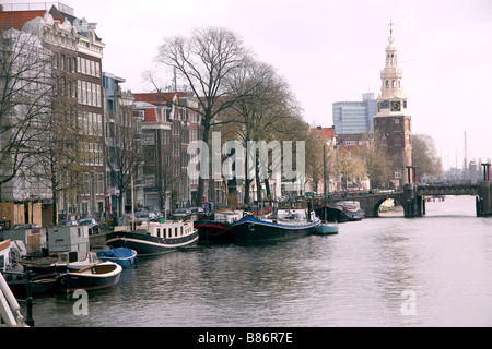 Boote und Lastkähne auf Amsterdam Canal mit Bridge und den Tower im Hintergrund Brücke in den Niederlanden Stockfoto