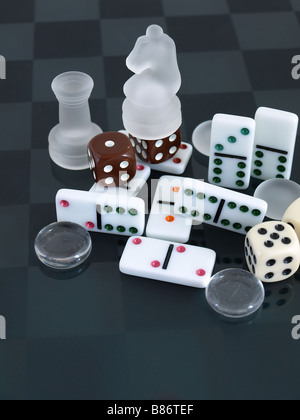 Mattiertes Glas Schach Stücke Dominos Würfel und Steinen angeordnet auf einem mattierten Checker board Stockfoto