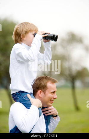 Vater mit Sohn auf Schultern Blick aber Fernglas Stockfoto