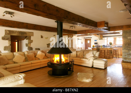 Wohnzimmer mit großen Ecksofa und zentralem Kamin mit brennenden Feuer und Ansichten durch zur Küche Stockfoto