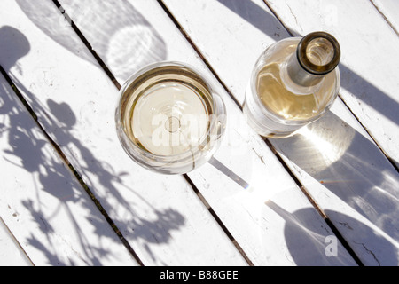 Eine Flasche Weißwein und ein Glas außen angebracht auf einem weißen Holztisch. Stockfoto