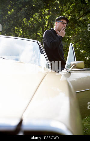 trendige Mann raucht eine Zigarre neben einem Oldtimer Stockfoto