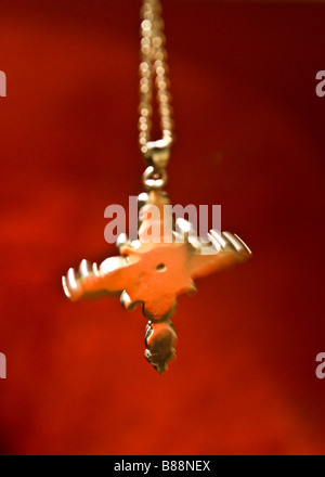 Ein heiliges Kreuz an einer Kette dreht sich gegen einen Hintergrund von rot. Stockfoto