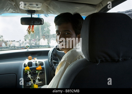 Indische Autofahrer / Fahrer lächelnd am Rücksitz Passagier; Toran Girlanden aus Ringelblumen sind ein Hindu Götter anzubieten. Surat, Indien Stockfoto