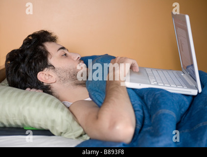 Ein junger Mann mit seinem Laptop während noch im Bett liegend. Stockfoto