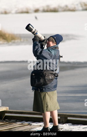 Eine Frau mittleren Alters mit einem Teleobjektiv fotografiert die Rotmilane in Nant yr Arian Wald Mitte Mitte Wales UK im Schnee Stockfoto