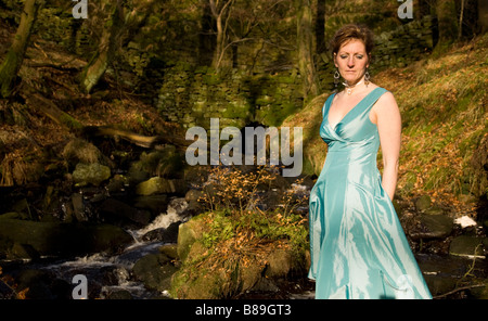 Eine attraktive Frau in einem wunderschönen blauen Kleid von einem Bergbach Stockfoto