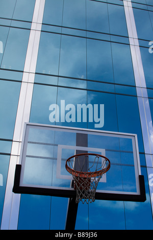 Basketballkorb mit Glas-Rückwand vor glatten Glas moderne Bürogebäude reflektierenden Wolken in der Oberfläche Stockfoto