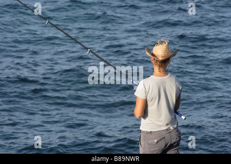 Rückansicht einer Frau, die Strohhutfischen von Felsen in Spanien trägt Stockfoto