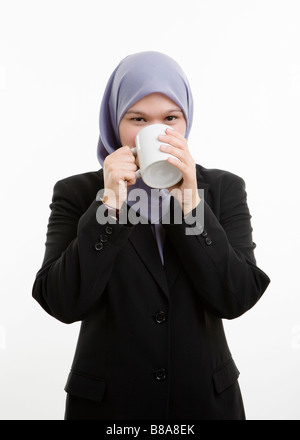 Exekutive Muslimin vor weißem Hintergrund stehen und eine Tasse Kaffee oder Tee trinken. Stockfoto