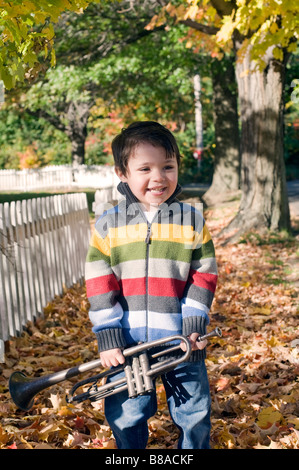 Drei Jahre alter Junge spielt mit seiner Trompete außerhalb an einem Herbsttag Stockfoto