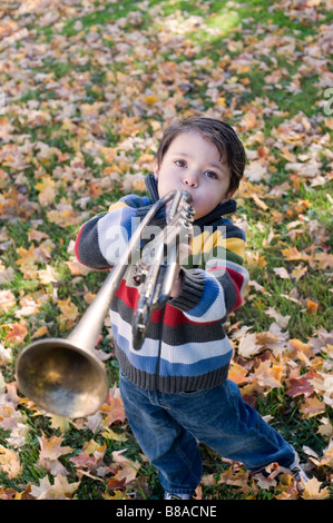 Drei Jahre alter Junge spielt mit seiner Trompete außerhalb an einem Herbsttag Stockfoto