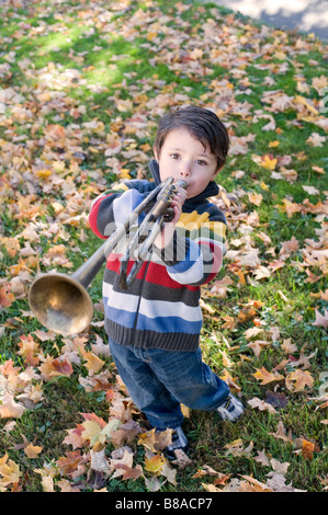 Drei Jahre alter Junge spielt mit seiner Trompete außerhalb an einem Herbsttag Stockfoto