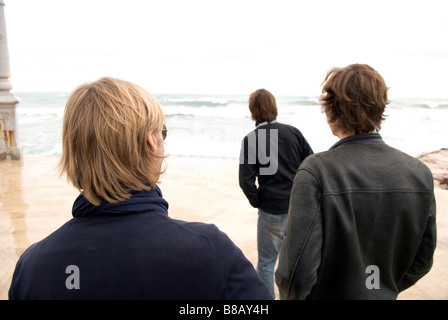 eine Rückansicht von drei erwachsenen Männern stehend auf einer Strandpromenade mit Blick auf das Meer an einem stürmischen Tag Stockfoto