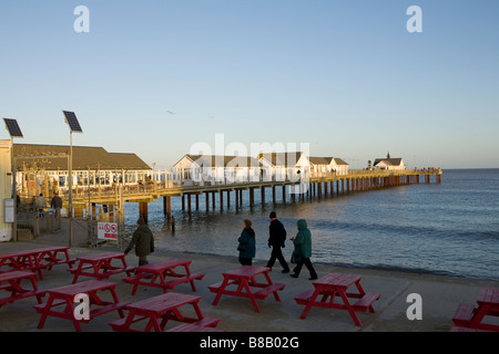 Wanderer auf Suffolks Southwold promenade mit Pier am Abend Sonnenlicht und rot Picknick-Tische im Vordergrund Stockfoto