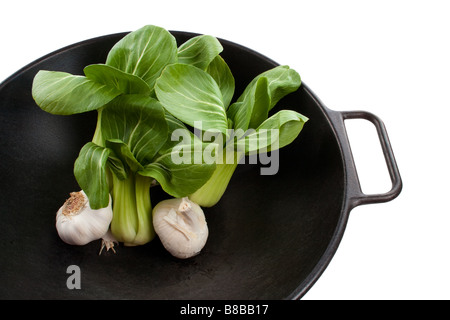 Stiele von Baby Bok Choy und zwei Köpfe von Knoblauch in einem schwarzen wok Stockfoto