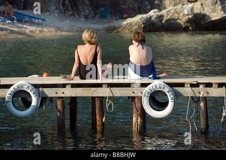 Nahaufnahme von zwei reifen Damen sitzen auf einem sonnigen Steg, Sonnenbaden im Taverna Agni Beach, Korfu, Kerkyra Griechenland Europa EU Stockfoto