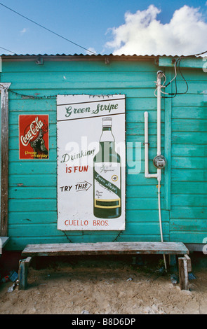 Vintage-Werbetafeln für Rum und Coca-Cola mit dem Slogan „Trinken ist Spaß“ an einer türkisfarbenen Holzwand in Caye Caulker, Belize, Mittelamerika. Stockfoto