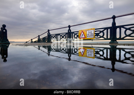 Die Buhnen Zeichen auf die dekorative Geländer auf der Promenade an der Brighton und Hove spiegelt sich in einer Pfütze fernzuhalten. Stockfoto