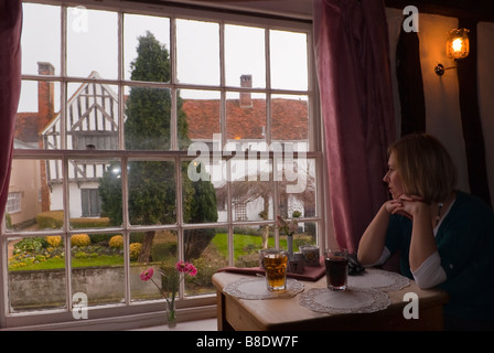 Eine junge Frau sitzt in einem Tee Zimmer Kaffee Schaufenster mit Blick auf einen malerischen Blick in Lavenham, Suffolk, Uk Stockfoto