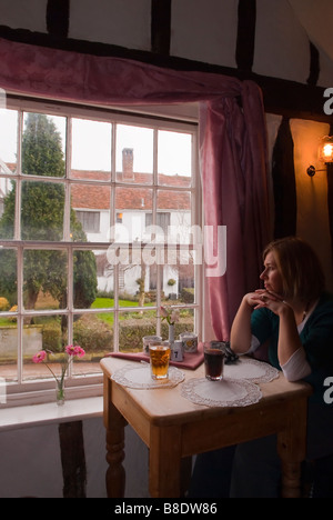Eine junge Frau sitzt in einem Tee Zimmer Kaffee Schaufenster mit Blick auf einen malerischen Blick in Lavenham, Suffolk, Uk Stockfoto