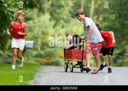 Kleinkinder mit Neufundländer Welpen Hund und roten Wagen in Wohnstraße im Sommer. Stockfoto