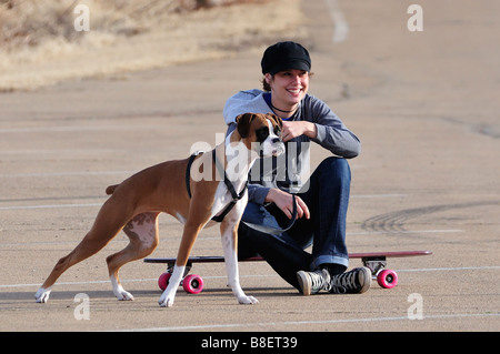 Ein hübsches Mädchen mit ihrem Boxer Hund an der Leine ruht auf ihrem Skateboard. Stockfoto