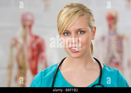 Eine schöne Ärztin in chirurgischen Peelings erschossen in einem Krankenhaus mit menschlichen Anatomie Poster unscharf hinter ihr Stockfoto