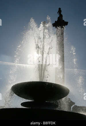 Sonne scheint durch einen Brunnen und Silhouetten Nelsonsäule am Trafalgar Square in London England UK Stockfoto