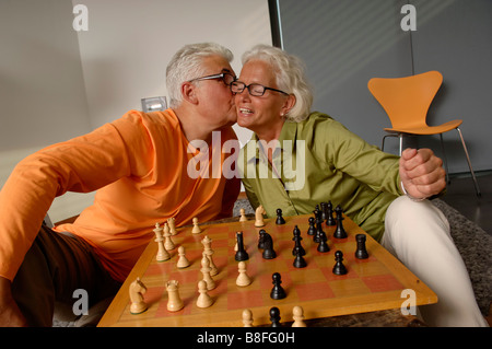 Ältere Mann küssen eine ältere Frau auf die Wange, Schachbrett vor Ihnen Stockfoto