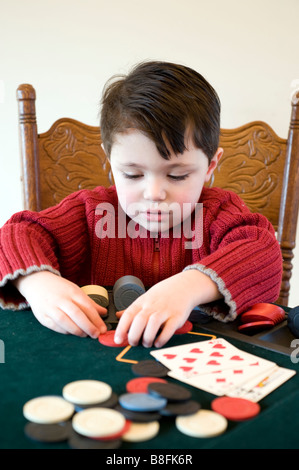 Junges Kind hält eine Hand Full House Poker und zieht in seine chips Stockfoto