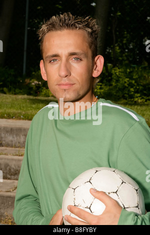 Junger Mann mit blonden Haaren hält einen Fußball, close-up Stockfoto