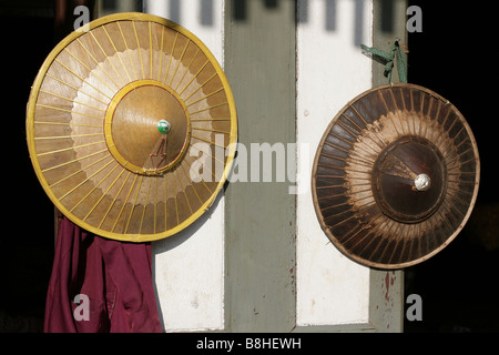 Traditionelle asiatische konische Hüte getragen von Menschen in Myanmar. Zwei Hüte asiatische von dünnen Streifen aus Bambus hängen an einer Wand in einer traditionellen Szene Stockfoto