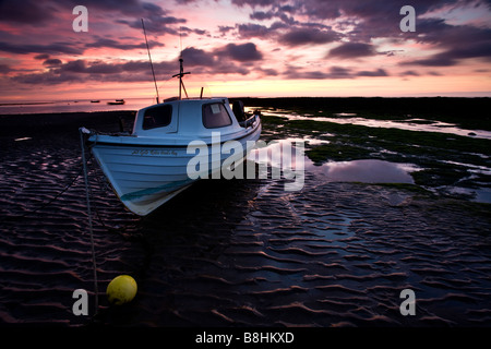 Ein kleines Fischerboot am Strand von Robin Hoods Bay bei Ebbe mit einem wunderschönen Sonnenaufgang Himmel Stockfoto