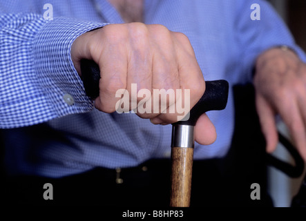 Älterer Mann mit einem blauen Hemd sitzt mit einem Rohrstock Stockfoto