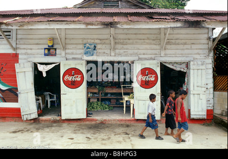 Drei Jungs laufen an einem mit Coca-Cola-Werbung geschmückten Eckgeschäft in der Stadt Livingston, Guatemala, vorbei. Stockfoto