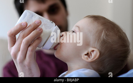 Ein kleinen Jungen ist Milch aus der Flasche gefüttert, auf seines Vaters Schoß liegend. Stockfoto